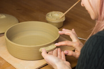 Woman ceramist attaching handle to the pot in pottery class. Potter workshop in ceramic studio