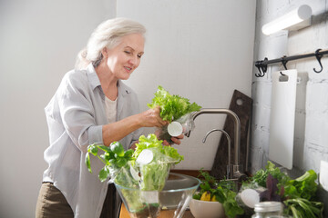 product delivery. healthy nutrition.  elderly womanwashes green salad in the kitchen at home. Senior lifestyle