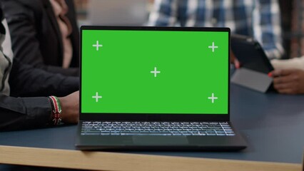 Canvas Print - Laptop display with green screen background on office desk, people attending business meeting. Isolated mockup template with blank chroma key and copy space on computer screen. Close up.