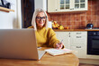 © baranq - Smiling mature woman making notes while calculating home finances