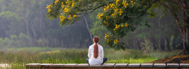 Panorama back view of woman relaxingly practicing meditation in the public park to attain happiness from inner peace wisdom with yellow flower blossom in summer