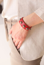 leather studded red bracelet on woman hand close up photo on white wall background