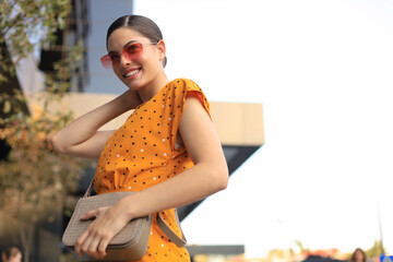 Portrait fashion woman in yellow dress walking on street of the city, smiling to side