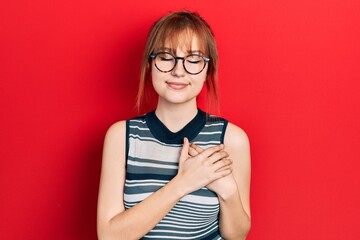 Sticker - Redhead young woman wearing casual clothes and glasses smiling with hands on chest with closed eyes and grateful gesture on face. health concept.