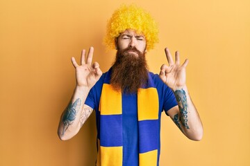 Wall Mural - Redhead man with long beard football hooligan cheering game wearing funny wig relax and smiling with eyes closed doing meditation gesture with fingers. yoga concept.