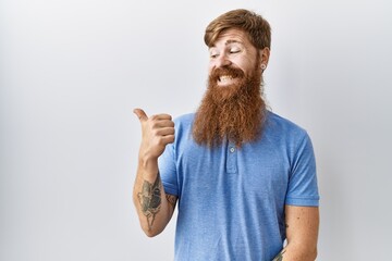 Sticker - Caucasian man with long beard standing over isolated background smiling with happy face looking and pointing to the side with thumb up.