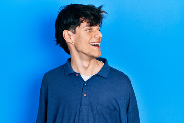 Sticker - Handsome hipster young man stranding over blue background looking away to side with smile on face, natural expression. laughing confident.