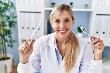 Canvas Print - Beautiful dentist woman holding ordinary toothbrush and electric toothbrush smiling with a happy and cool smile on face. showing teeth.