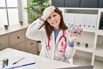 Canvas Print - Young doctor woman holding sweets candy stressed and frustrated with hand on head, surprised and angry face