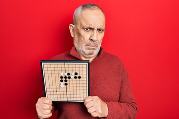 Canvas Print - Handsome mature man holding asian go game board skeptic and nervous, frowning upset because of problem. negative person.