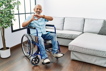 Wall Mural - Handsome senior man sitting on wheelchair at the living room smiling in love doing heart symbol shape with hands. romantic concept.