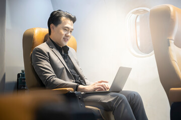 young asian businessman sitting in airplane cabin business class and chatting online, checking email