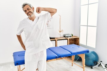 Sticker - Middle age hispanic therapist man working at pain recovery clinic stretching back, tired and relaxed, sleepy and yawning for early morning