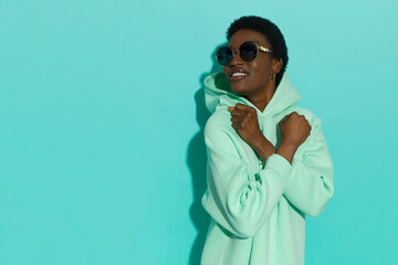 Happy young black woman in pastel mint sweatshirt and sunglasses is looking to the side.