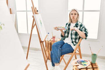 Sticker - Young artist woman painting on canvas at art studio puffing cheeks with funny face. mouth inflated with air, crazy expression.