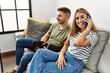 © Krakenimages.com - Young hispanic couple smiling happy talking on the smartphone sitting on the sofa with dog at home.