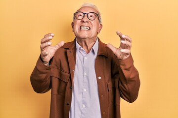 Wall Mural - Senior man with grey hair wearing casual jacket and glasses crazy and mad shouting and yelling with aggressive expression and arms raised. frustration concept.