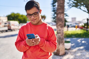 Down syndrome man smiling confident using smartphone at park