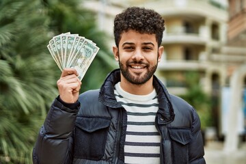 Canvas Print - Young arab man holding United Arab Emirates dirham banknotes outdoor at the town