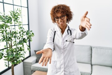 Wall Mural - Young african american woman wearing doctor uniform and stethoscope looking at the camera smiling with open arms for hug. cheerful expression embracing happiness.