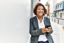 Middle Age Latin Businesswoman Smiling Happy Using Smartphone At The City.