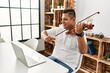 © Krakenimages.com - Young hispanic man having online violin lesson using laptop sitting on the table at home.