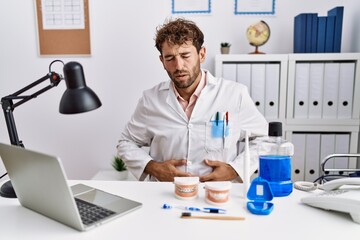 Canvas Print - Young hispanic dentist man working at medical clinic with hand on stomach because indigestion, painful illness feeling unwell. ache concept.