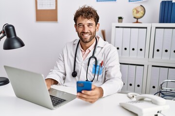 Poster - Young hispanic man wearing doctor uniform using smartphone at clinic