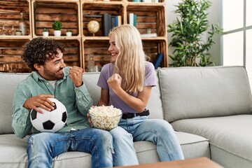 Poster - Young couple watching soccer match eating porpcorn at home.