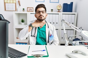 Canvas Print - Young man with beard wearing doctor uniform and stethoscope at the clinic cutting throat with hand as knife, threaten aggression with furious violence