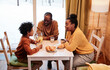 Young happy family of three communicating by breakfast while sitting by table served with homemade snacks in their country house