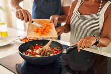 Middle Age Hispanic Couple Pouring Food On Frying Pan At Kitchen