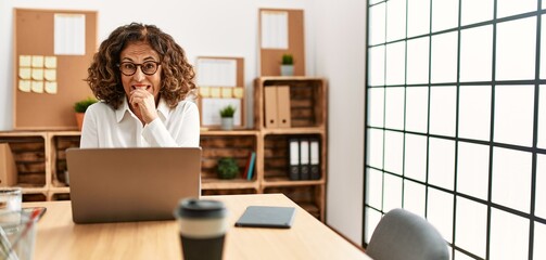 Canvas Print - Middle age hispanic woman working at the office wearing glasses looking stressed and nervous with hands on mouth biting nails. anxiety problem.