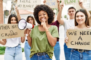 Sticker - Group of young friends protesting and giving slogans at the street serious face thinking about question with hand on chin, thoughtful about confusing idea