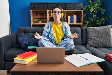 Poster - Young hispanic woman studying using computer laptop and headphones making fish face with mouth and squinting eyes, crazy and comical.