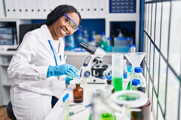 Sticker - African american woman wearing scientist uniform pouring liquid on bottle laboratory