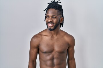 Wall Mural - African man with dreadlocks standing shirtless over isolated background looking away to side with smile on face, natural expression. laughing confident.