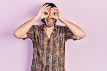 Poster - Middle age caucasian man wearing casual clothes doing ok gesture like binoculars sticking tongue out, eyes looking through fingers. crazy expression.