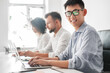 Leinwandbild Motiv Smiling Asian male employee working on laptop near diverse colleagues in office