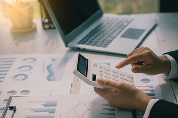 Wall Mural - Businessman's hands pressing a calculator, calculating, analyzing, graphing, charting, accounting worker working on a laptop. A bank clerk who advises making financial reports or company profits.