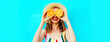 Summer portrait of happy cheerful smiling woman covering her eyes with slices of orange and looking for something wearing straw hat on blue background