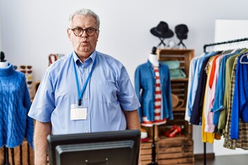 Wall Mural - Senior man with grey hair working as manager at retail boutique making fish face with lips, crazy and comical gesture. funny expression.