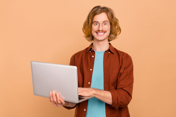 Poster - Portrait of handsome cheerful skilled trendy red-haired guy holding using laptop isolated over beige pastel color background