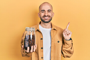 Sticker - Young bald man holding jar of raisins smiling happy pointing with hand and finger to the side