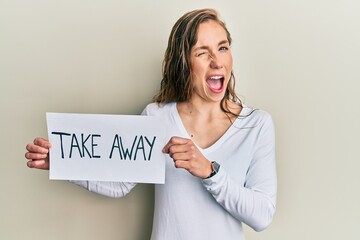 Wall Mural - Young blonde woman holding take away food winking looking at the camera with sexy expression, cheerful and happy face.