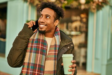 Young african american man talking on the smartphone and drinking coffee at the city