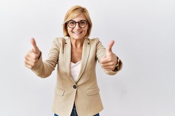 Sticker - Middle age blonde business woman standing over isolated background approving doing positive gesture with hand, thumbs up smiling and happy for success. winner gesture.