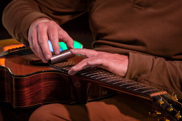 Guitariste jouant sur sa guitare folk posée à plat avec un bottleneck en fer. Gros plan réalisé pendant un concert.