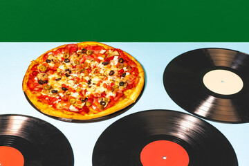 Food pop art photography. Italian pizza lying on vinyl discs on light tablecloth isolated on green background. Vintage, retro style fashion, music