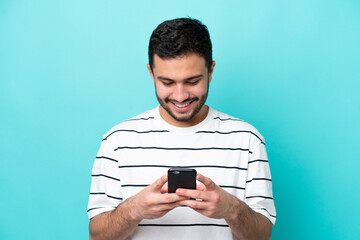 Wall Mural - Young Brazilian man isolated on blue background sending a message or email with the mobile